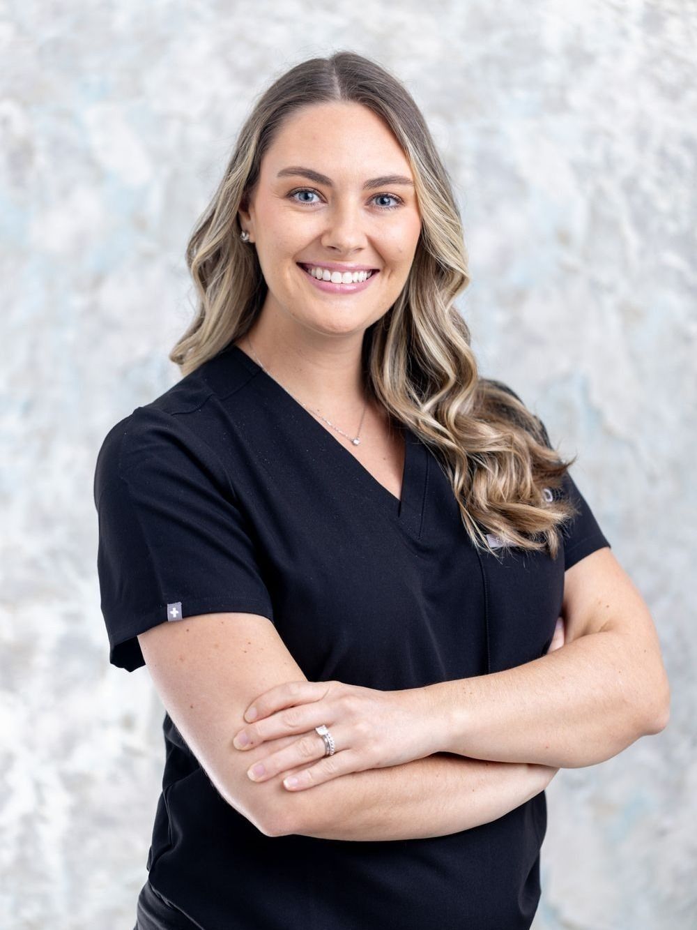 aesthetic physician associate brook buchanan smiling in black scrubs with folded arms.