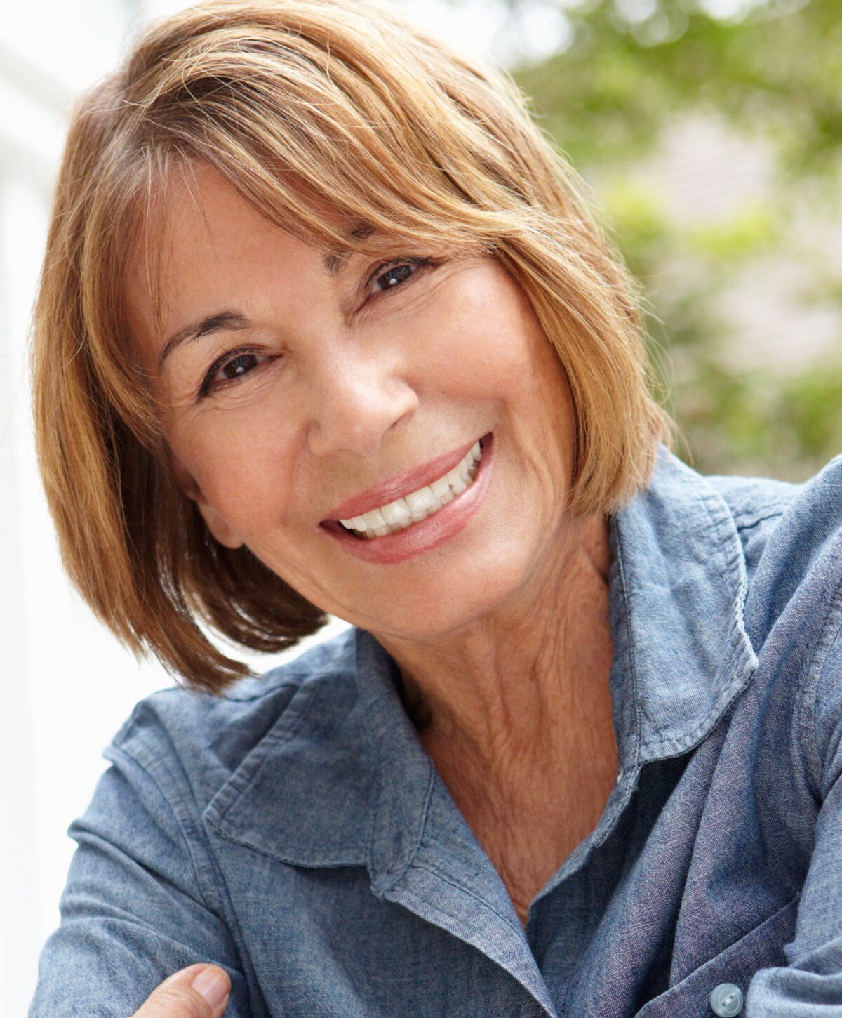 Smiling botox patient model in denim shirt outdoors.