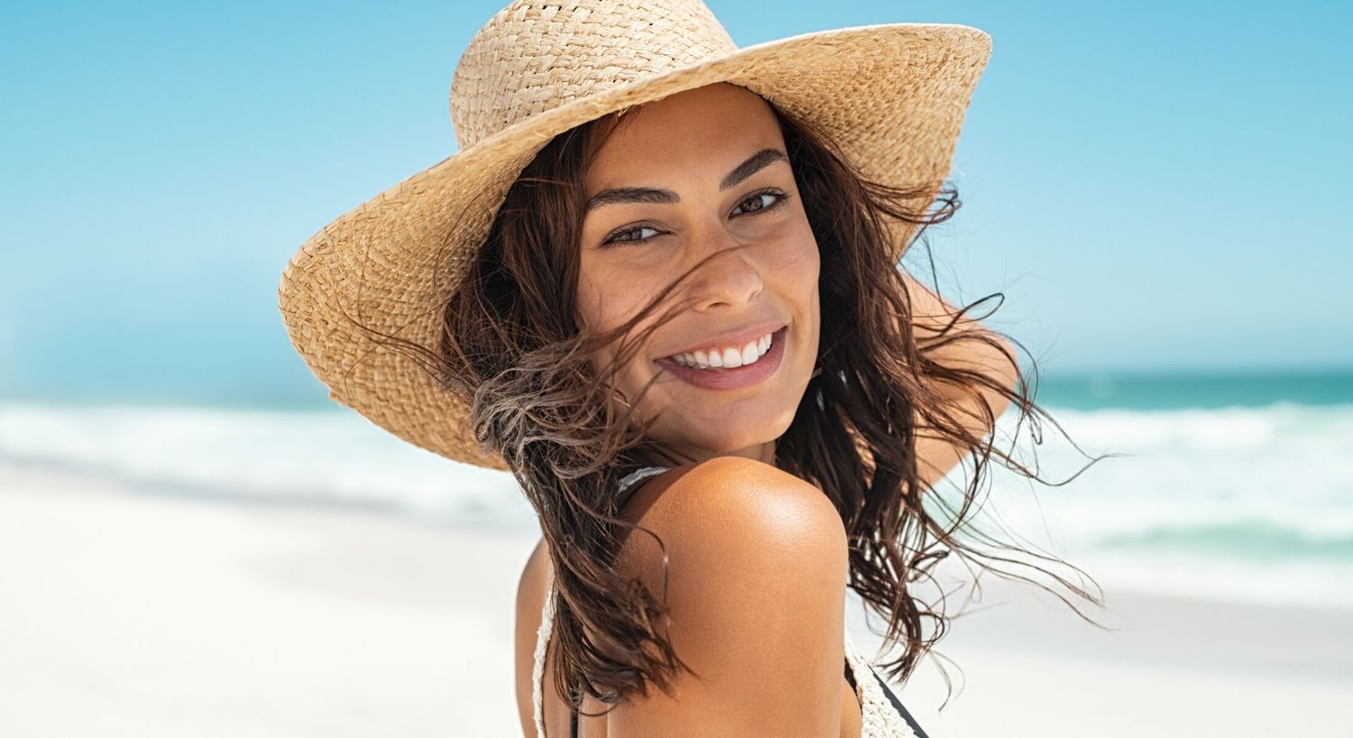 Smiling exosome therapy patient model in straw hat at beach.