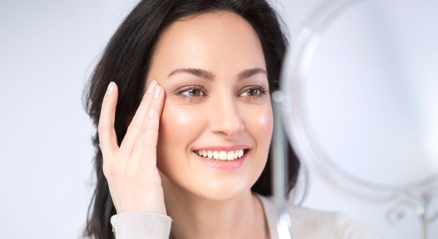 Facial patient model looking in a mirror and smiling while touching her temple