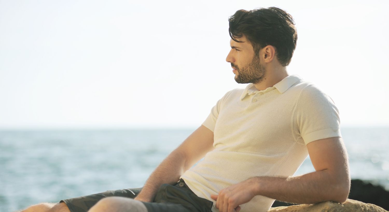 Ozone Therapy patient model in a polo shirt reclining on some rocks by the ocean
